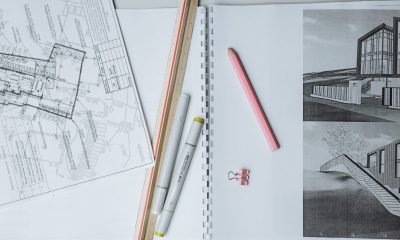 Flat lay of architectural blueprints, drawing tools, and stationery on a desk surface.