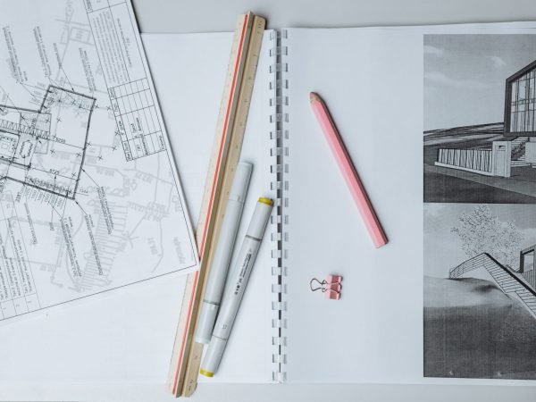 Flat lay of architectural blueprints, drawing tools, and stationery on a desk surface.